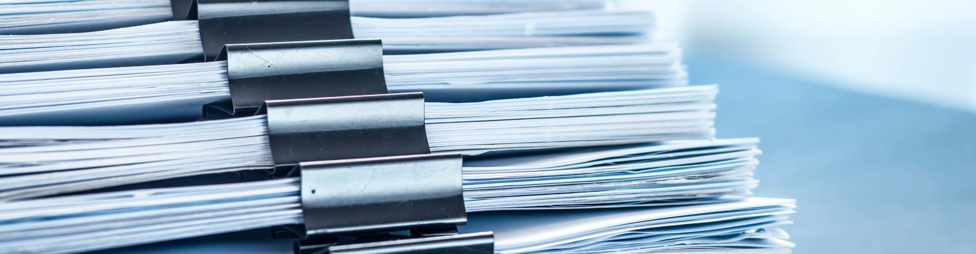 Plusieurs dossiers papier tenus avec des pinces
