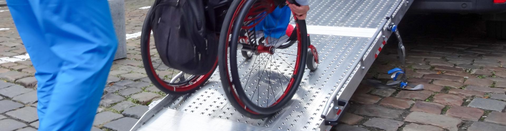 Personne qui pousse une autre personne en fauteuil roulant sur une rampe d'accès d'un véhicule