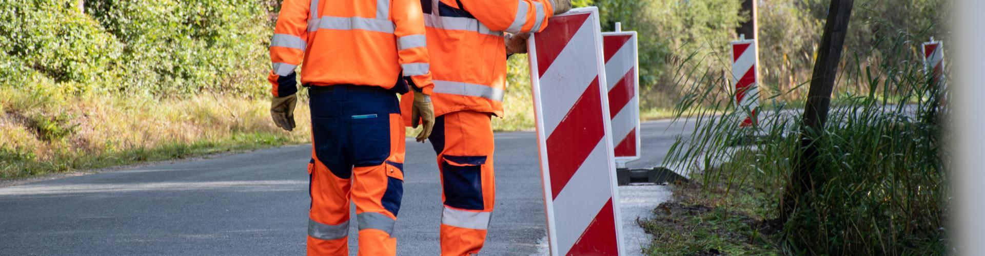 Deux hommes installent des panneaux de travaux sur une route