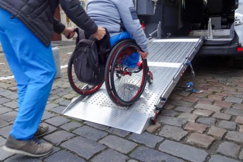 Personne qui pousse une autre personne en fauteuil roulant sur une rampe d'accès d'un véhicule